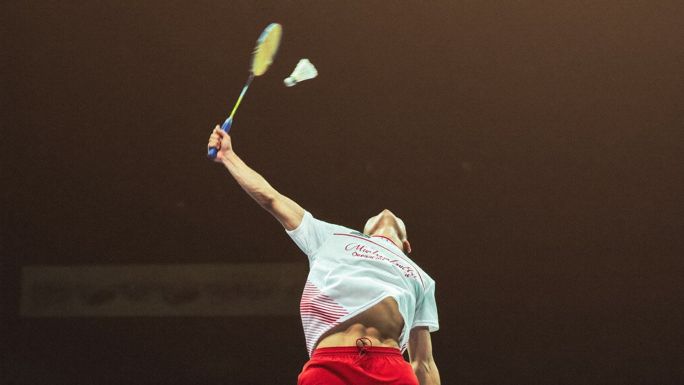 Badminton player mid jump smash in a packed arena