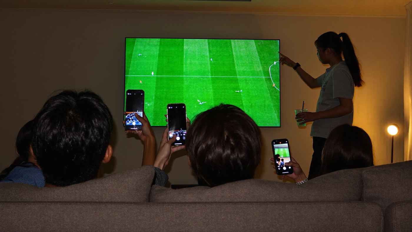 Family and friends watching sport on television at home with phones in hand